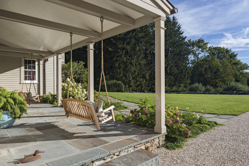 Photo of an expansive traditional front veranda in New York with natural stone paving and a roof extension.