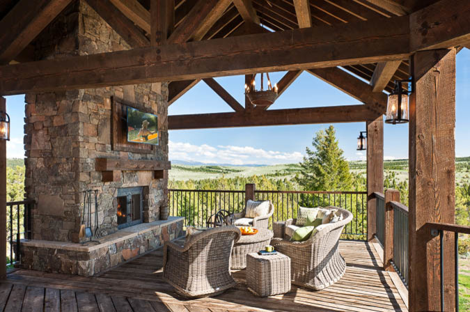 Cette photo montre un grand porche d'entrée de maison arrière montagne avec un foyer extérieur, une terrasse en bois et une extension de toiture.