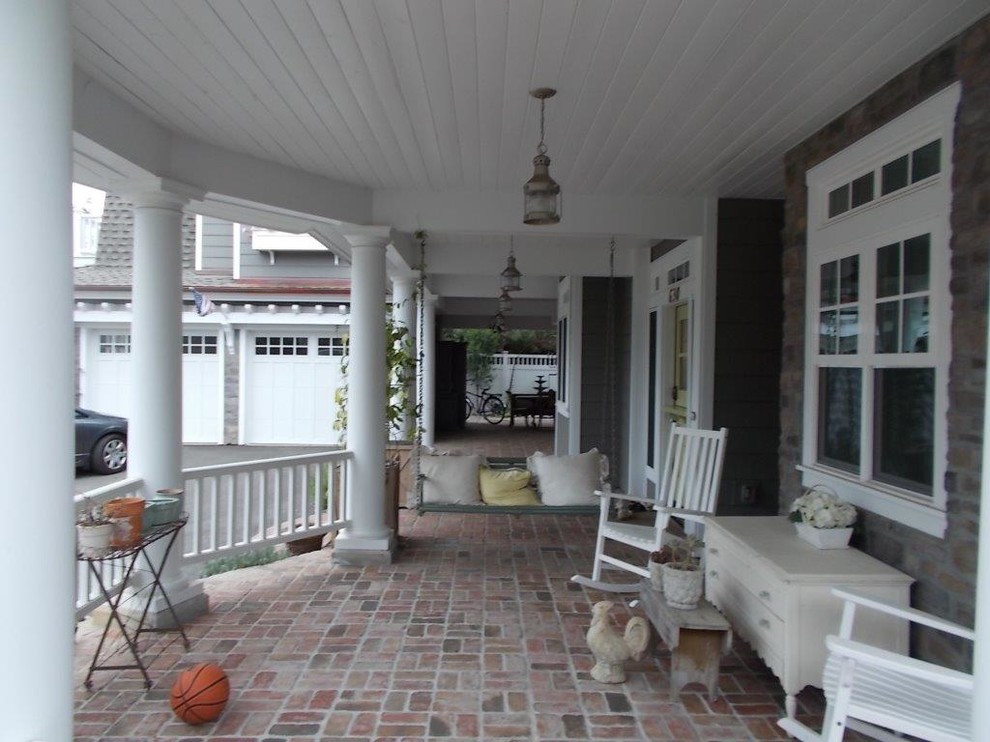 Immagine di un portico country di medie dimensioni e davanti casa con pavimentazioni in mattoni, un tetto a sbalzo e con illuminazione