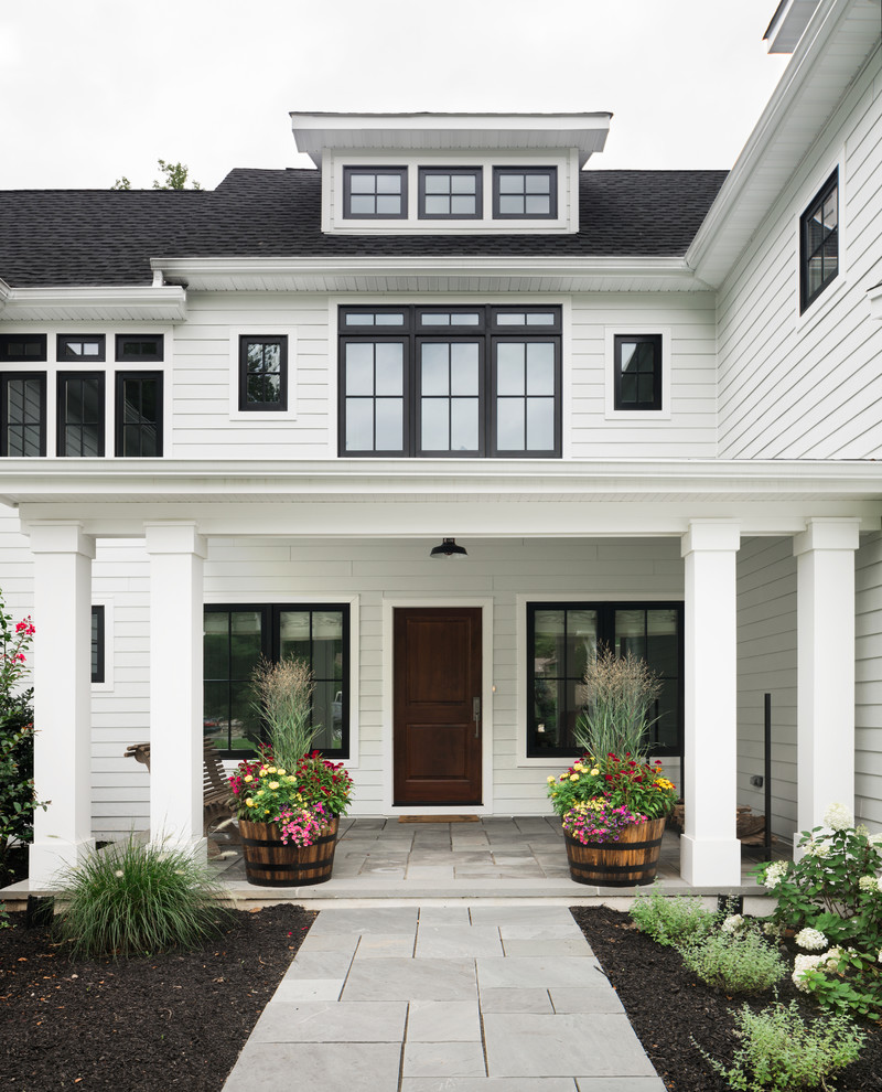 This is an example of a large beach style front veranda in New York with a roof extension and concrete paving.