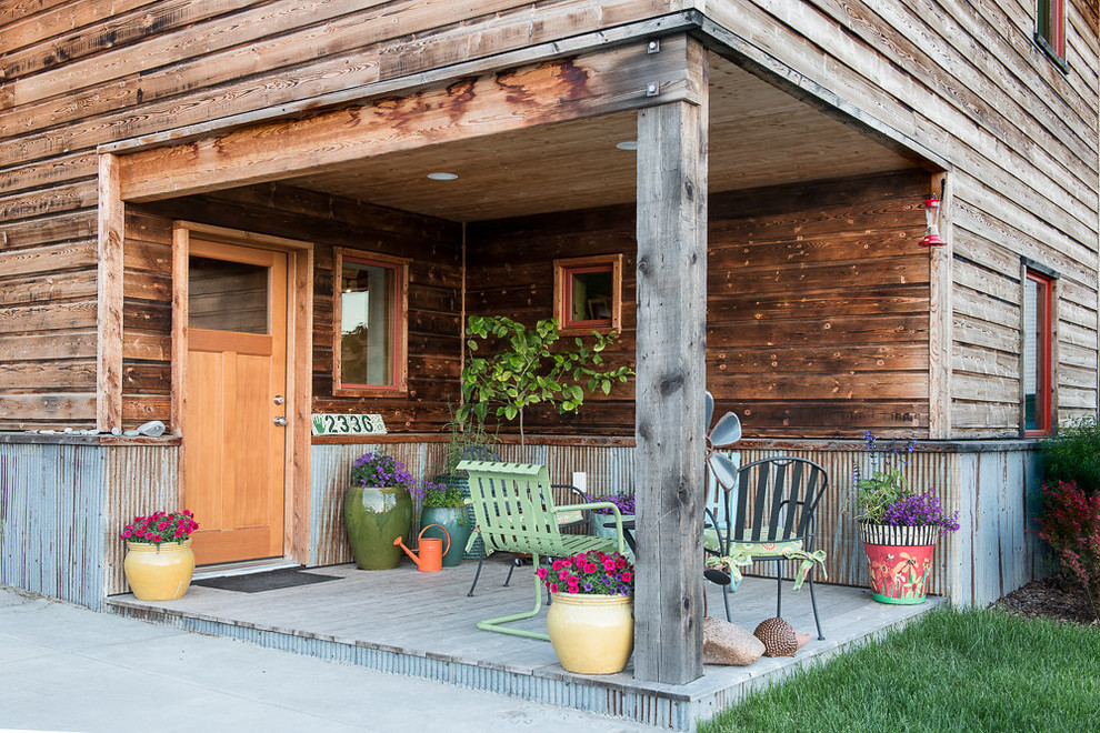Rustik inredning av en liten veranda framför huset, med trädäck, takförlängning och utekrukor