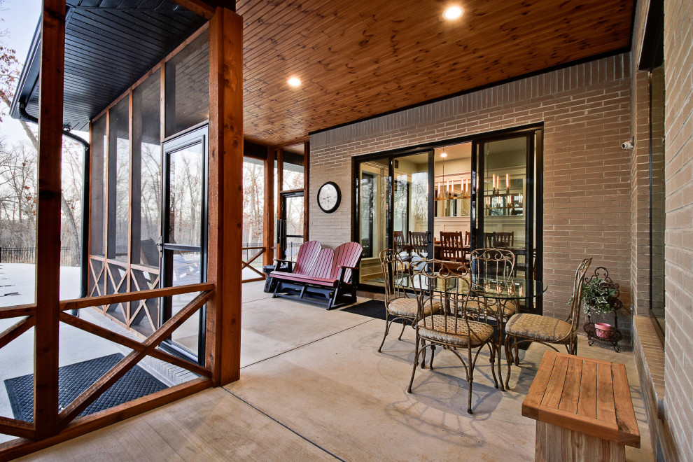 This is an example of a large modern concrete screened-in back porch design in Other with a roof extension.