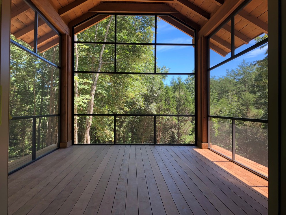 Cette photo montre un porche d'entrée de maison arrière avec une extension de toiture, un garde-corps en métal, une moustiquaire et une terrasse en bois.