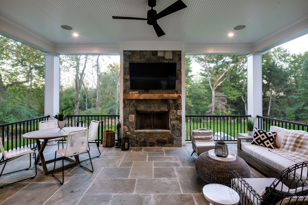Cette image montre un grand porche d'entrée de maison arrière craftsman avec une cheminée, des pavés en pierre naturelle et une extension de toiture.