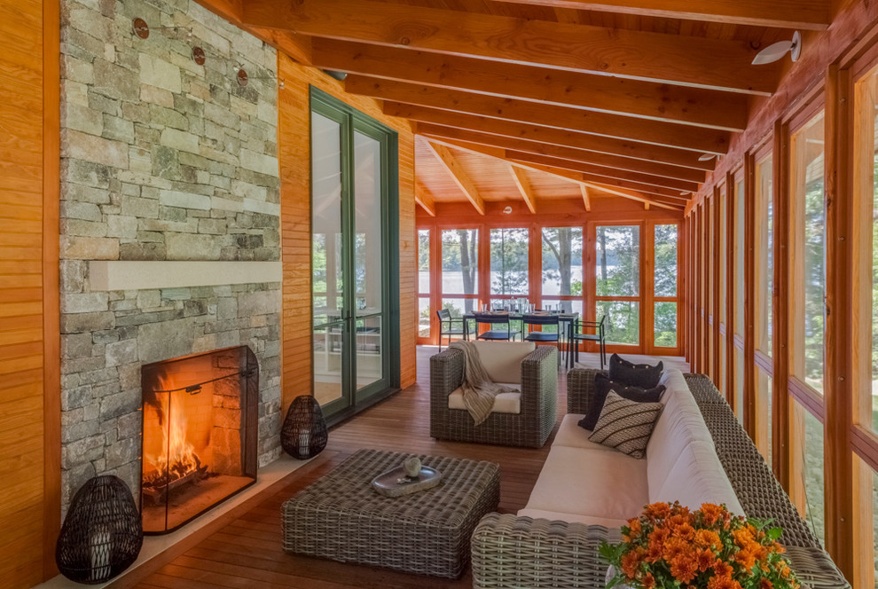 Cette image montre un grand porche d'entrée de maison latéral chalet avec un foyer extérieur, une terrasse en bois, une extension de toiture et tous types de couvertures.