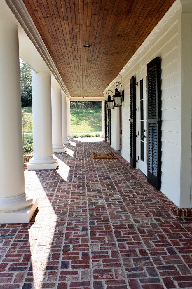Exempel på en stor klassisk veranda framför huset, med marksten i tegel och takförlängning