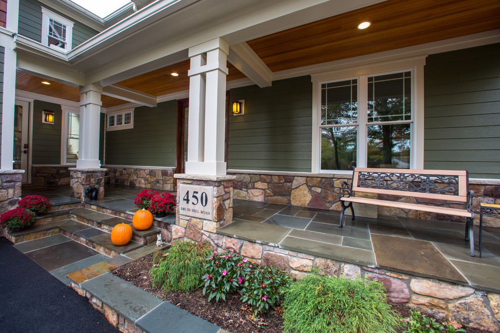Foto di un grande portico stile americano davanti casa con pavimentazioni in pietra naturale e un tetto a sbalzo