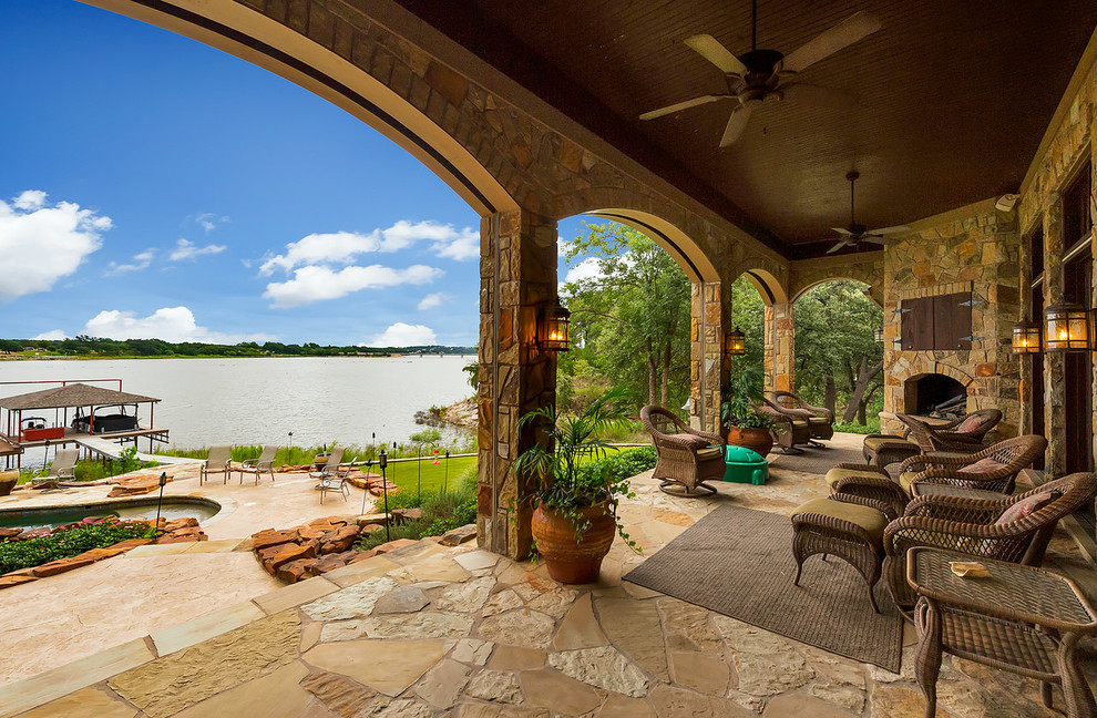 This is an example of a large mediterranean stone back porch design in Dallas with a fireplace and a roof extension.