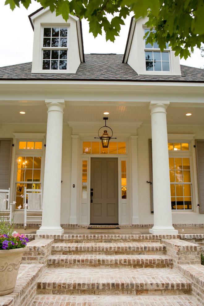 This is an example of a large traditional brick front porch design in New Orleans with a roof extension.