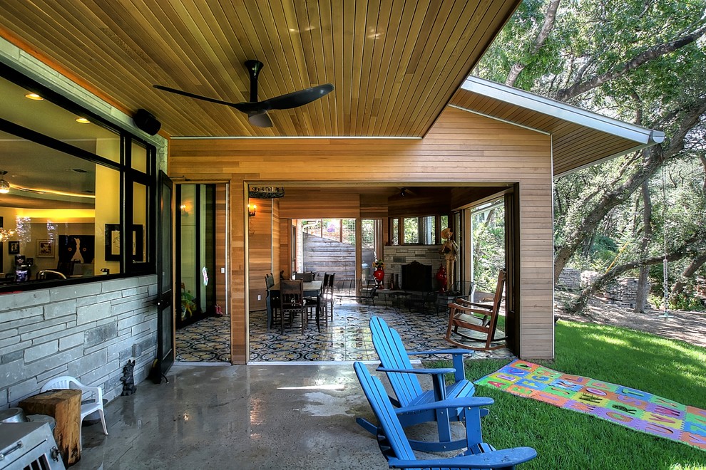 Cette image montre un grand porche d'entrée de maison arrière bohème avec un foyer extérieur, une dalle de béton et une extension de toiture.