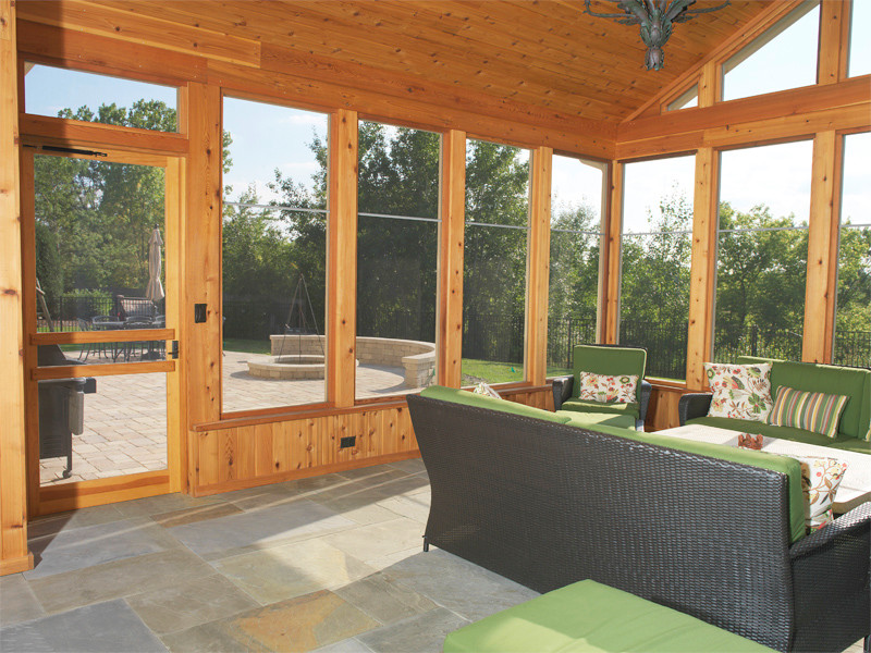 Cette image montre un grand porche d'entrée de maison arrière bohème avec une moustiquaire, des pavés en pierre naturelle et une extension de toiture.