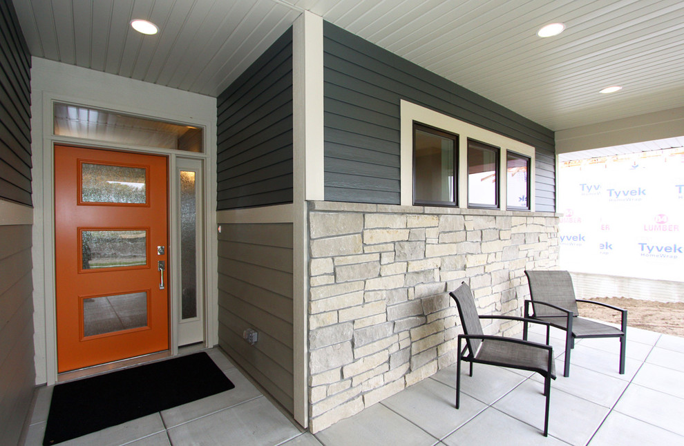 This is an example of a mid-sized 1960s concrete paver front porch design in Omaha with a roof extension.