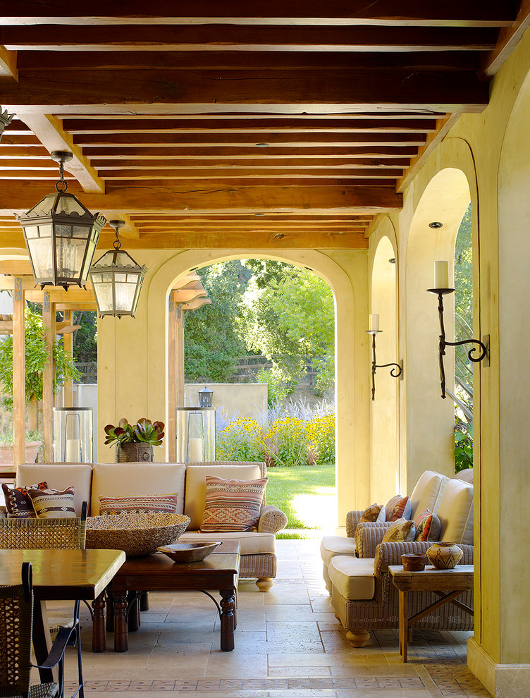 Cette image montre un grand porche d'entrée de maison arrière méditerranéen avec une extension de toiture et des pavés en pierre naturelle.
