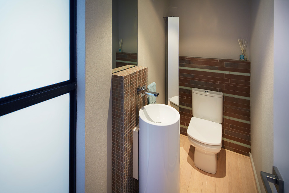Стильный дизайн: туалет среднего размера в современном стиле с раковиной с пьедесталом, стеклянными фасадами, унитазом-моноблоком, плиткой мозаикой, бежевыми стенами и коричневой плиткой - последний тренд
