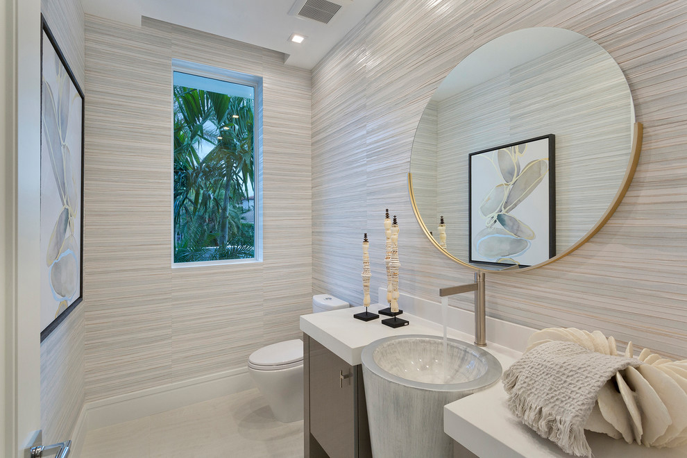 Modern inredning av ett mellanstort vit vitt toalett, med släta luckor, beige väggar, marmorgolv, ett nedsänkt handfat, bänkskiva i akrylsten, beiget golv och grå skåp