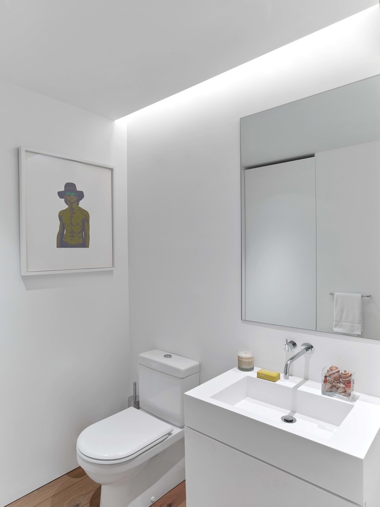 Idées déco pour un WC et toilettes moderne avec un placard à porte plane, des portes de placard blanches, un mur blanc, un sol en bois brun, un plan vasque et un sol marron.