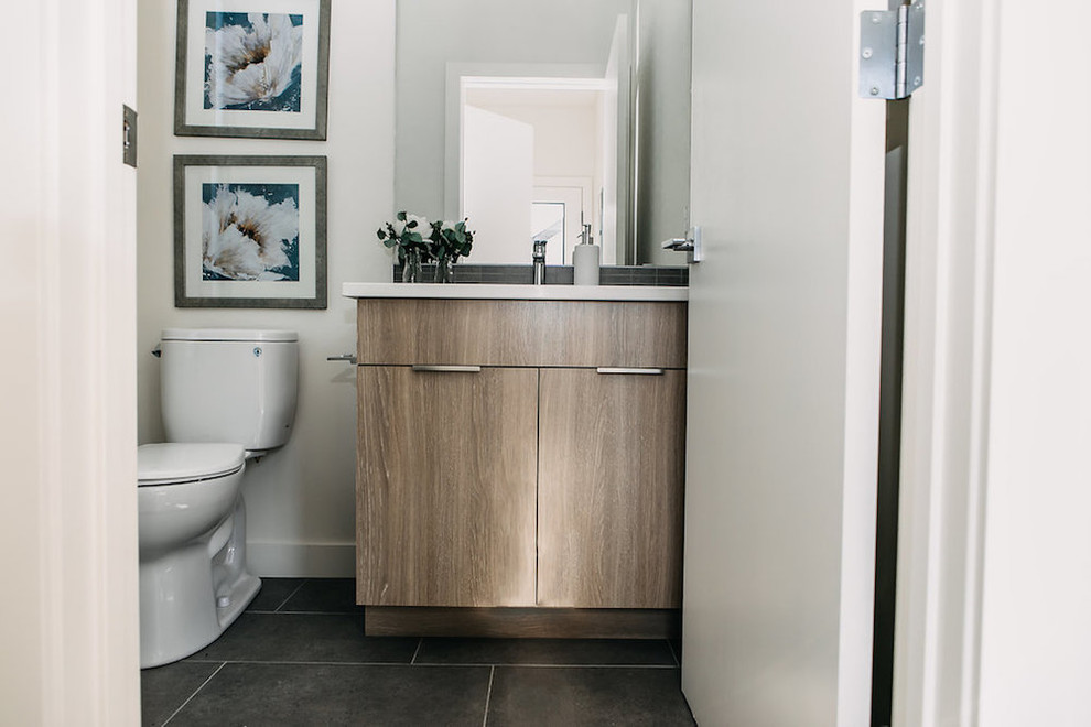 Immagine di un bagno di servizio moderno di medie dimensioni con ante in stile shaker, ante in legno chiaro, WC monopezzo, pareti bianche, lavabo sottopiano, pavimento nero e top bianco