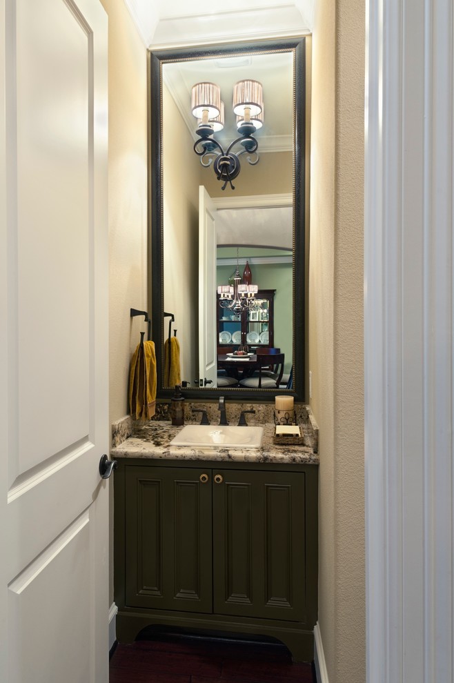 Diseño de aseo tradicional pequeño con armarios con rebordes decorativos, puertas de armario verdes, paredes beige, suelo de madera oscura, lavabo encastrado y encimera de granito