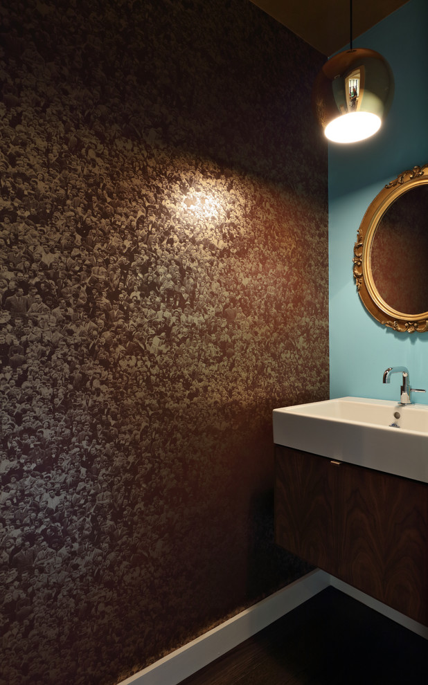Inspiration for a small modern cloakroom in New York with dark wood cabinets, dark hardwood flooring, solid surface worktops, blue walls, a wall-mounted sink, a floating vanity unit, wallpapered walls and a wall mounted toilet.