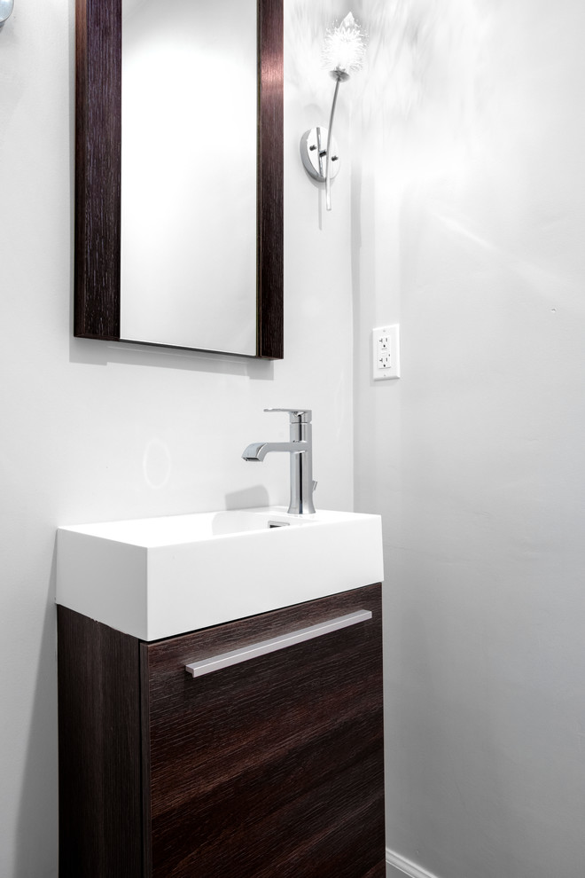 Bild på ett litet vit vitt toalett, med släta luckor, skåp i mörkt trä, en vägghängd toalettstol, flerfärgad kakel, porslinskakel, grå väggar, ljust trägolv, ett integrerad handfat, bänkskiva i akrylsten och beiget golv