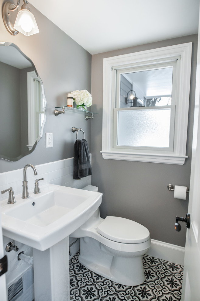 Klassisk inredning av ett mellanstort toalett, med en toalettstol med hel cisternkåpa, vit kakel, keramikplattor, grå väggar, cementgolv, ett piedestal handfat, bänkskiva i akrylsten och flerfärgat golv