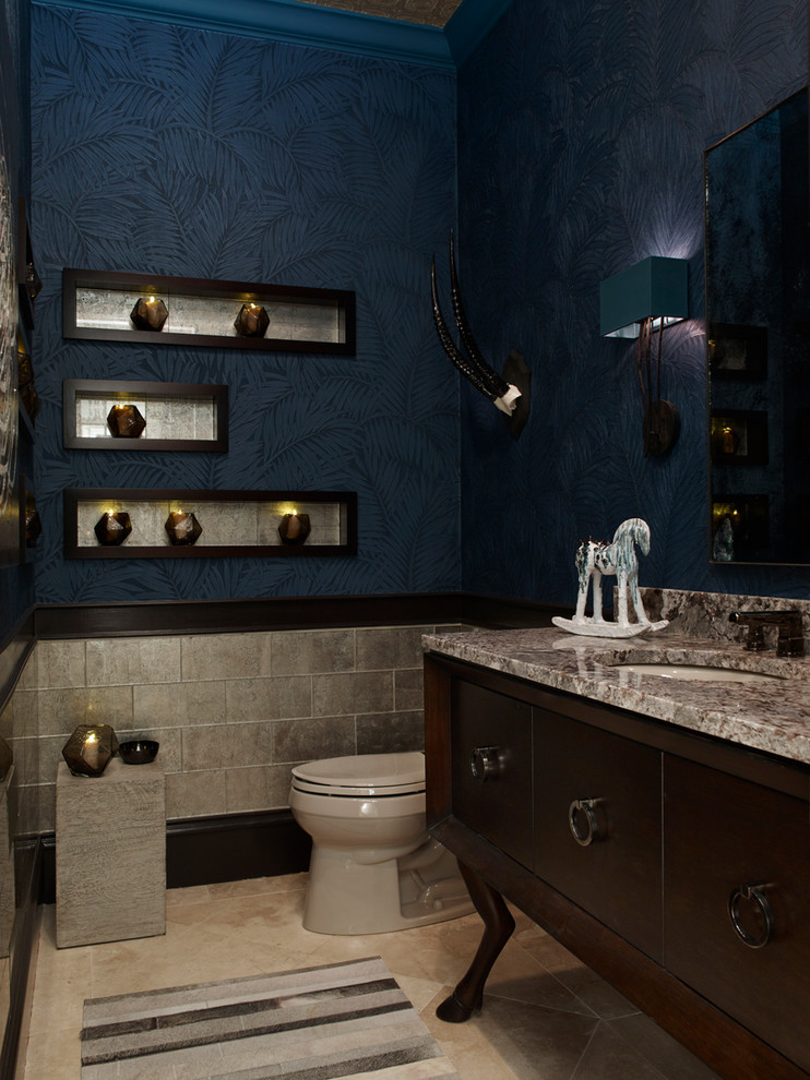 Bild på ett litet vintage toalett, med ett undermonterad handfat, skåp i mörkt trä, granitbänkskiva, en toalettstol med hel cisternkåpa, flerfärgad kakel, glaskakel, blå väggar och kalkstensgolv