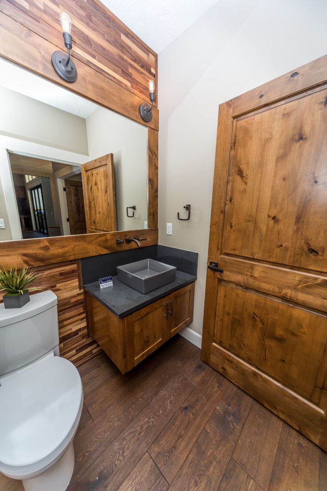 Cette image montre un WC et toilettes chalet en bois brun de taille moyenne avec un placard à porte shaker, WC séparés, un mur beige, un sol en bois brun, une vasque et un plan de toilette en béton.