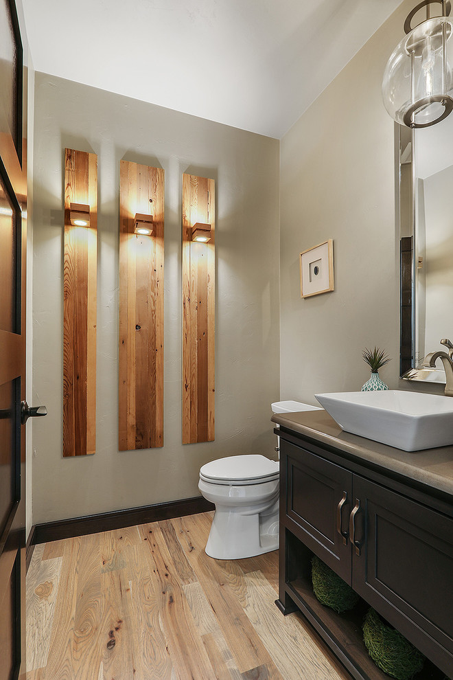 Klassisk inredning av ett stort toalett, med möbel-liknande, skåp i mörkt trä, grå väggar, ljust trägolv, ett fristående handfat, bänkskiva i kvartsit, brunt golv och en toalettstol med separat cisternkåpa