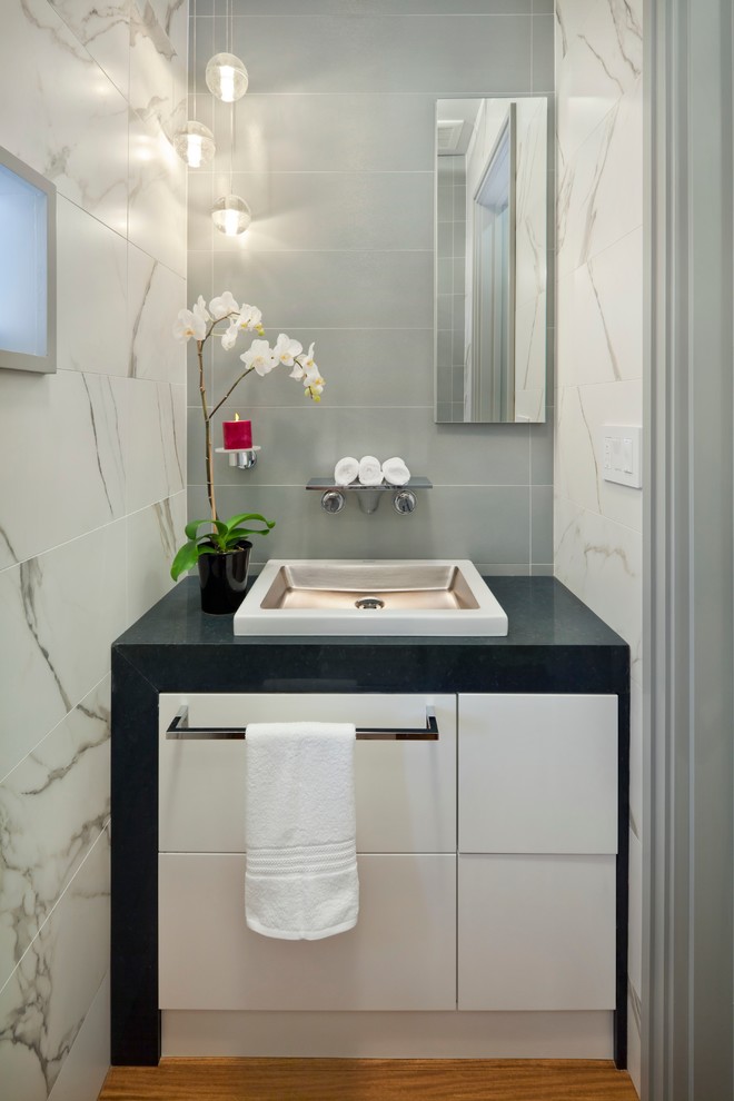 Foto på ett mellanstort funkis grå toalett, med ett fristående handfat, släta luckor, vita skåp, grå kakel, bänkskiva i kvarts, porslinskakel, grå väggar och ljust trägolv