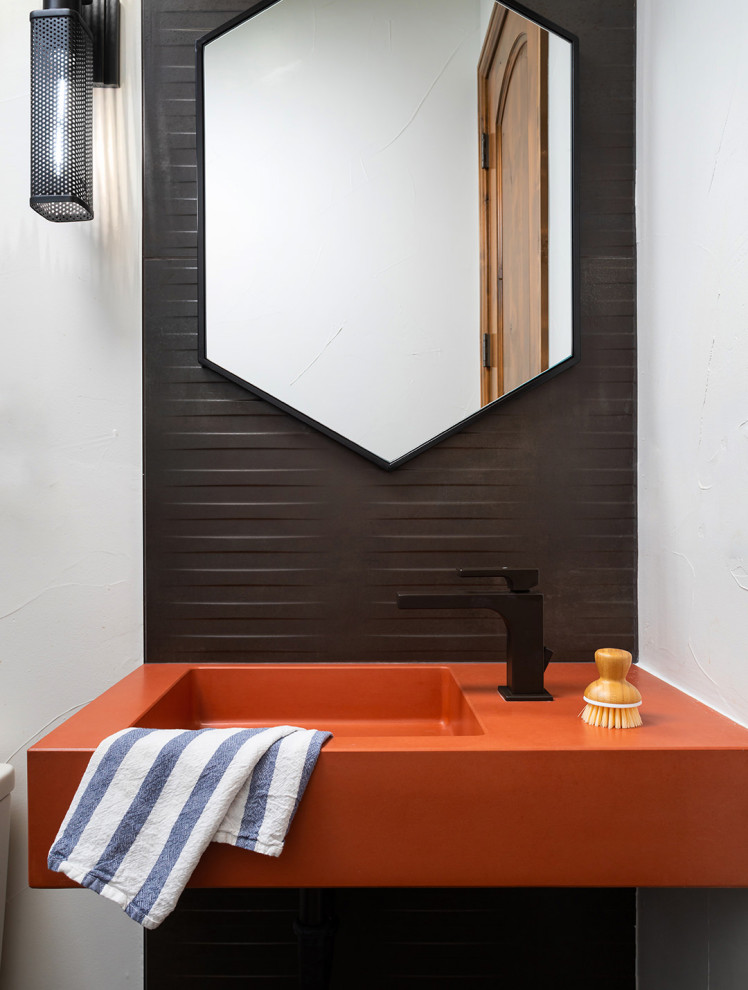 Bild på ett litet funkis orange oranget toalett, med orange skåp, en toalettstol med hel cisternkåpa, svart kakel, keramikplattor, vita väggar, klinkergolv i keramik, ett konsol handfat, bänkskiva i betong och grått golv