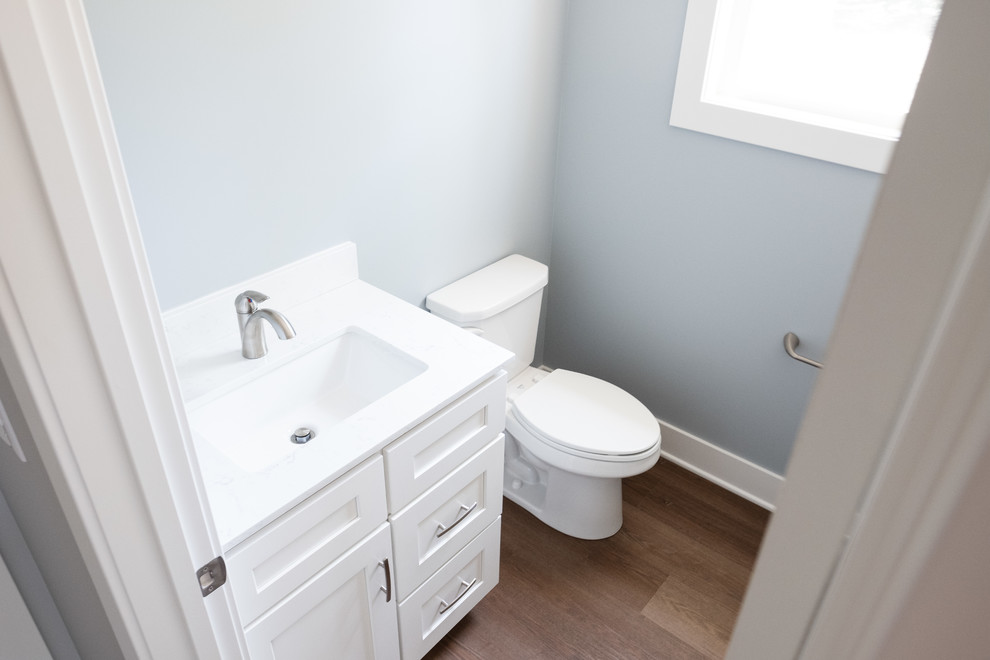 Design ideas for a small classic cloakroom in Grand Rapids with shaker cabinets, white cabinets, a two-piece toilet, blue walls, dark hardwood flooring, a submerged sink, quartz worktops, brown floors and white worktops.