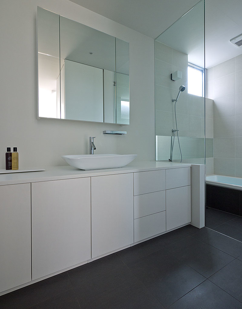Diseño de cuarto de baño minimalista de tamaño medio con lavabo sobreencimera, armarios con paneles lisos, puertas de armario blancas, sanitario de una pieza, baldosas y/o azulejos grises, paredes blancas y suelo de baldosas de cerámica