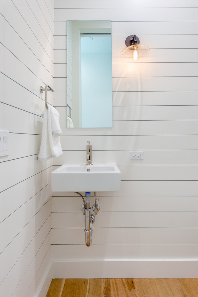 Diseño de aseo clásico renovado con paredes blancas, suelo de madera clara y lavabo suspendido