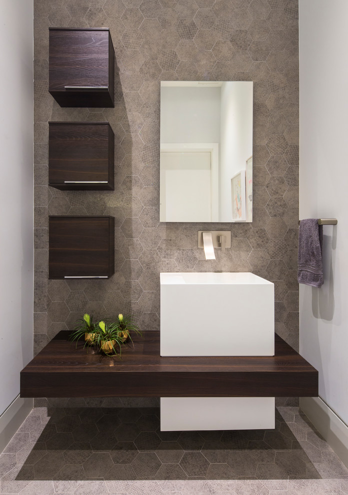 Exemple d'un WC et toilettes tendance de taille moyenne avec un carrelage gris, des carreaux de porcelaine, un sol en carrelage de porcelaine, un lavabo suspendu, un plan de toilette en bois et un plan de toilette marron.