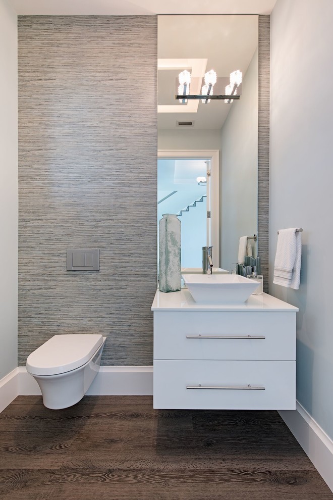 Exemple d'un WC suspendu tendance avec un placard à porte plane, des portes de placard blanches, un mur gris, une vasque, un sol marron et un plan de toilette blanc.