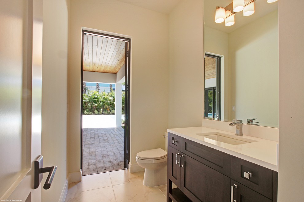 Example of a mid-sized tuscan powder room design in Miami with dark wood cabinets, a wall-mount toilet, beige walls and quartzite countertops