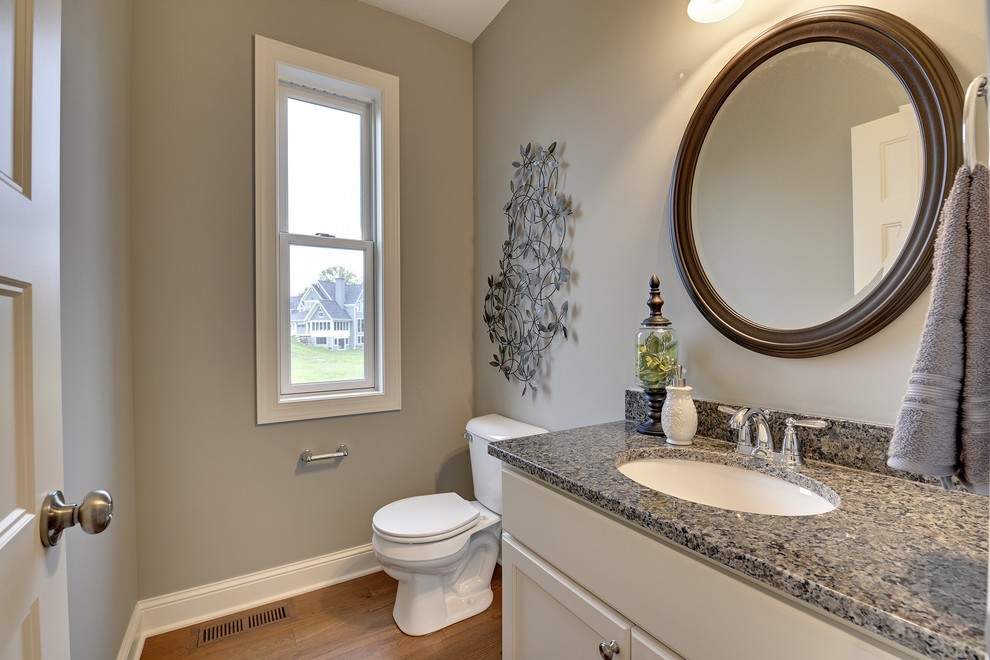 Powder room - small transitional medium tone wood floor powder room idea in Minneapolis with an undermount sink, recessed-panel cabinets, white cabinets, granite countertops, a one-piece toilet and gray walls