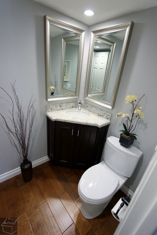 Foto på ett litet vintage toalett, med ett undermonterad handfat, luckor med infälld panel, skåp i mörkt trä, granitbänkskiva, en toalettstol med separat cisternkåpa och grå väggar
