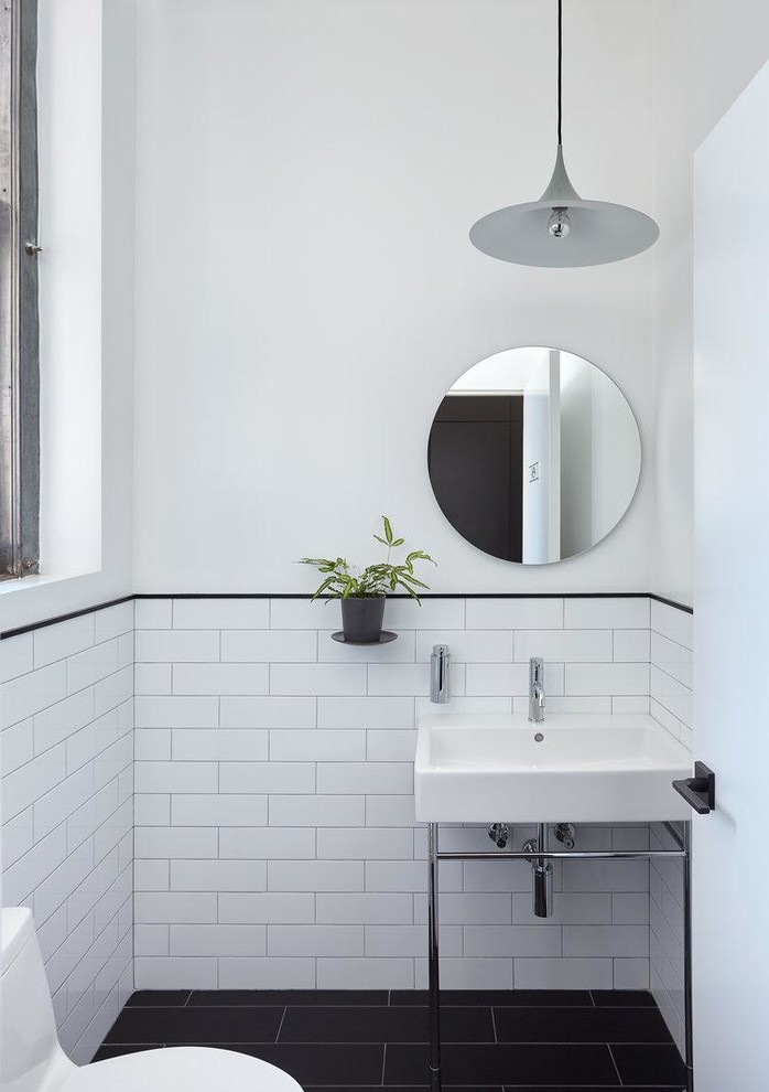 ニューヨークにある小さなトランジショナルスタイルのおしゃれなトイレ・洗面所 (一体型トイレ	、白いタイル、サブウェイタイル、白い壁、磁器タイルの床、コンソール型シンク、黒い床) の写真