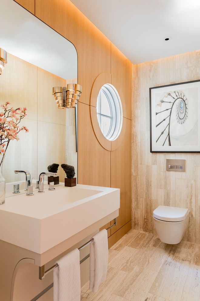 Inredning av ett modernt toalett, med en vägghängd toalettstol, beige kakel, ett väggmonterat handfat, travertinkakel och beiget golv