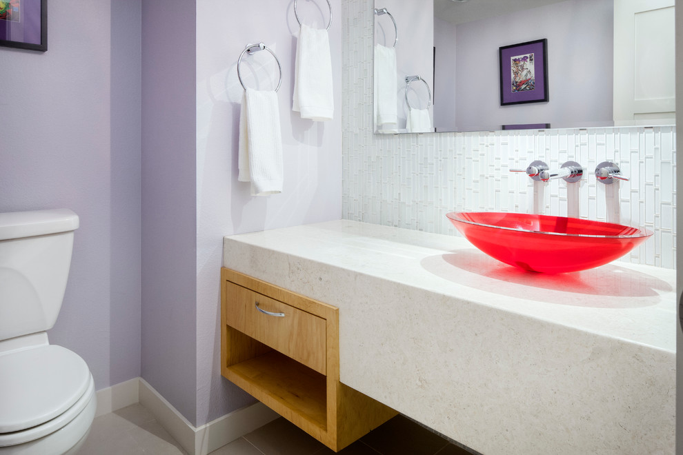 Modelo de aseo actual con lavabo sobreencimera, encimera de mármol, baldosas y/o azulejos de vidrio, paredes púrpuras, puertas de armario de madera clara y baldosas y/o azulejos blancos