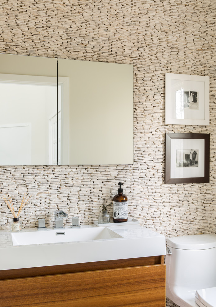 Cette photo montre un WC et toilettes tendance en bois brun de taille moyenne avec un placard à porte plane, WC à poser, un carrelage beige, un carrelage de pierre, un mur beige, un plan de toilette en marbre, un plan de toilette blanc et un lavabo intégré.