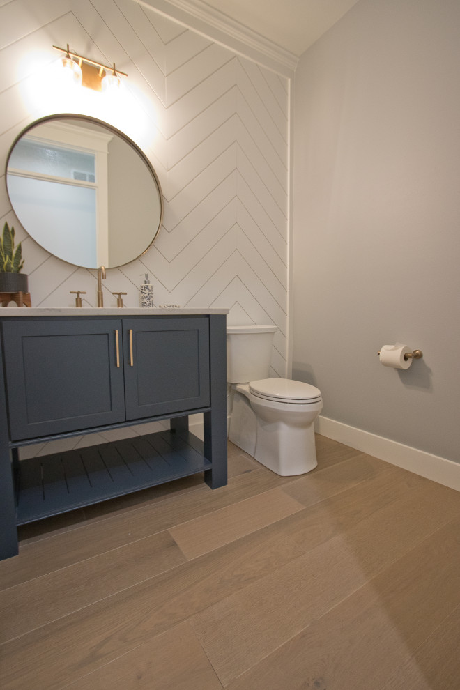 Powder room - french country light wood floor, brown floor and shiplap wall powder room idea in Other with recessed-panel cabinets, blue cabinets, a two-piece toilet, white walls, quartz countertops, white countertops and a freestanding vanity