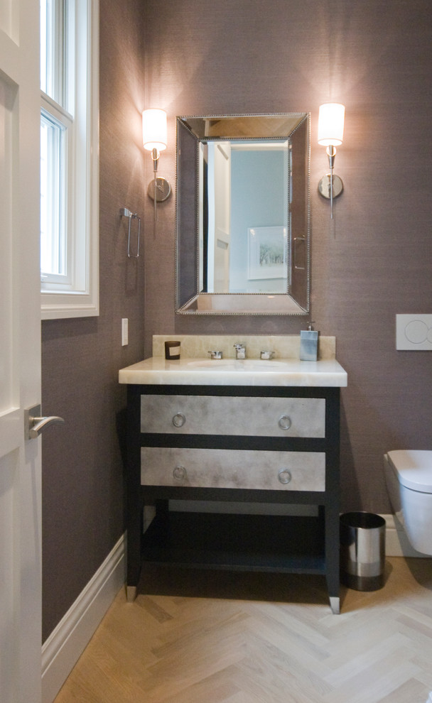 Cette image montre un WC suspendu traditionnel avec un lavabo encastré, un placard à porte plane, un plan de toilette en marbre, un mur violet, parquet clair et des portes de placard grises.