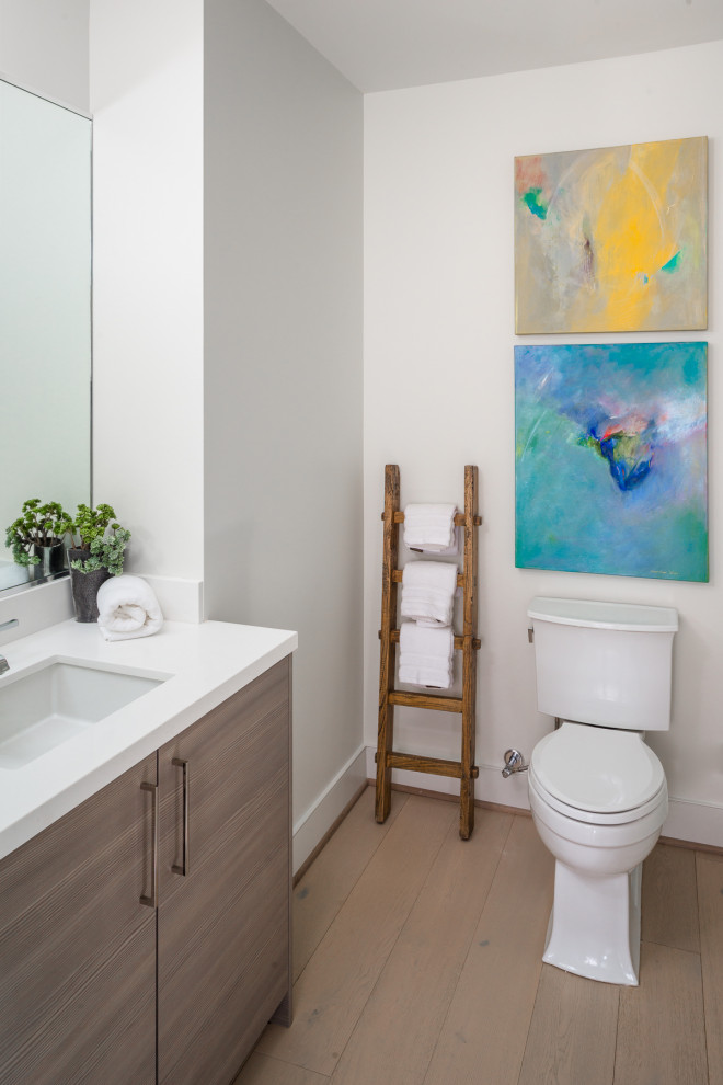 Inspiration for a contemporary cloakroom in Houston with flat-panel cabinets, medium wood cabinets, a two-piece toilet, white walls, light hardwood flooring, a submerged sink, beige floors and white worktops.