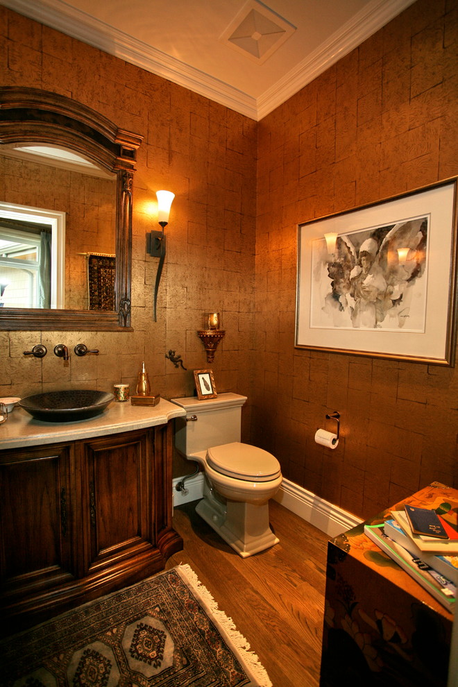 На фото: туалет в классическом стиле с настольной раковиной, фасадами с утопленной филенкой, столешницей из искусственного камня, унитазом-моноблоком, разноцветными стенами, темным паркетным полом и темными деревянными фасадами с