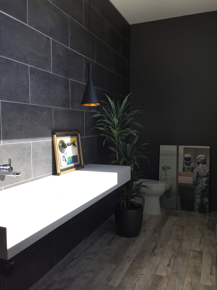 This is an example of a medium sized modern cloakroom in Los Angeles with a two-piece toilet, grey tiles, grey walls, light hardwood flooring, a trough sink and stone tiles.