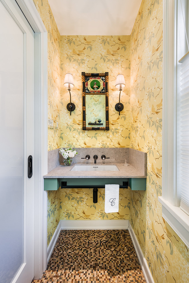 Lantlig inredning av ett litet toalett, med en toalettstol med hel cisternkåpa, beige kakel, gula väggar, mosaikgolv, ett undermonterad handfat och bänkskiva i kvarts