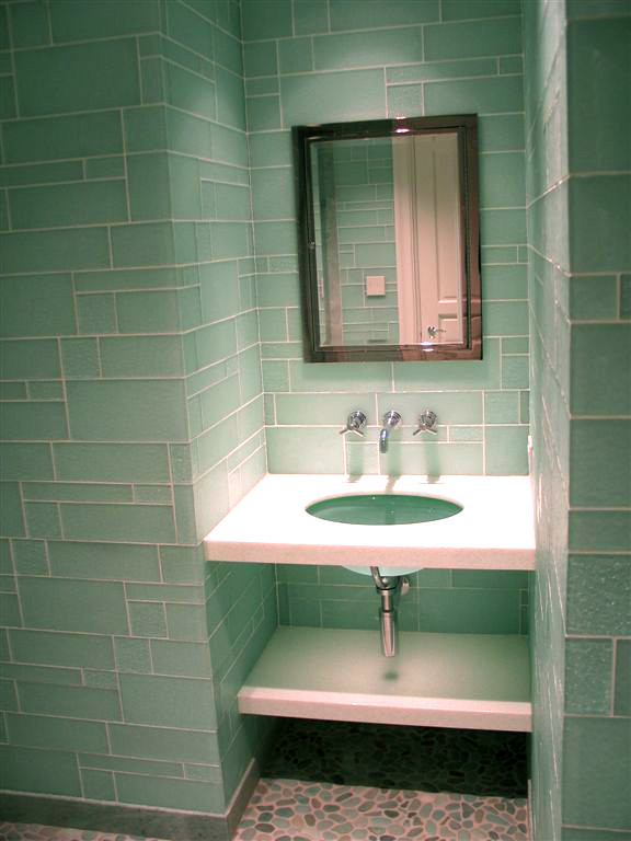 Inredning av ett modernt mellanstort toalett, med öppna hyllor, vita skåp, en toalettstol med hel cisternkåpa, grön kakel, glaskakel, gröna väggar, klinkergolv i småsten, ett undermonterad handfat, bänkskiva i akrylsten och flerfärgat golv