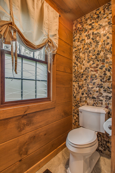 Rustik inredning av ett litet toalett, med släta luckor, bruna skåp, en toalettstol med separat cisternkåpa, flerfärgad kakel, stenkakel, bruna väggar, klinkergolv i keramik, ett nedsänkt handfat, granitbänkskiva och grått golv
